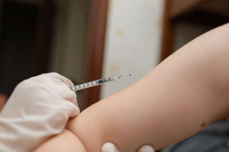 Young girl receiving vaccination immunisation by doctor, focus on shoulder. Medical syringe with vaccine. Health care and medicine concept.の写真素材