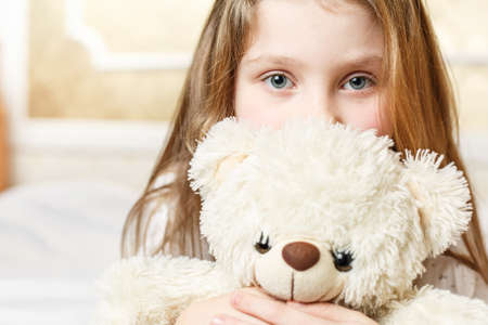 cute little girl is lying with a soft toy on a clean white soft bed, healthy sleep in a child is good healthの写真素材
