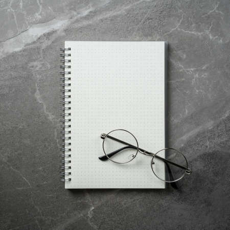 open notebook with glasses on grey marble table top view, spiral notepad on gray office desktop....