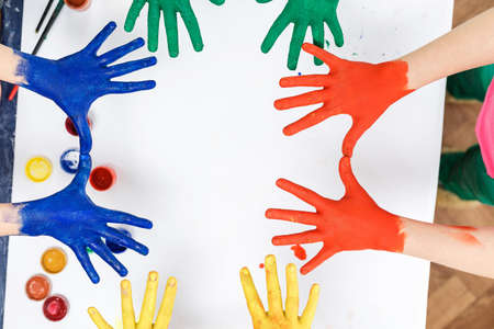 hands in paints on the background of a light table painted in different colors, children's hands soiled in gouache paint top viewの写真素材