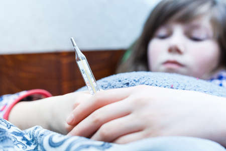 child is measured by the temperature of a thermometer, a cold and the flu is at home with a high temperature, the doctor checks the patient, the temperature is 38 on a thermometerの写真素材
