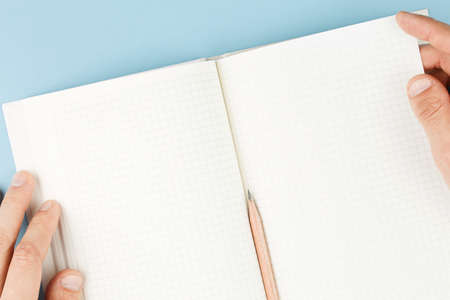 notepad in his hands on blue background top view, boy writes into the notebook the to-do list for...