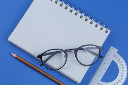 school notebook with pen and glasses on a blue table, top view, office desktop, office supplies on a...