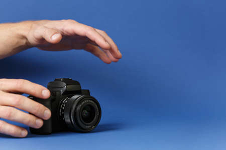 Male hands take a digital camera on a blue background front view.の写真素材