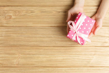 gift box in the hands on a wooden background top view, flat lay festive concept, female hands with...