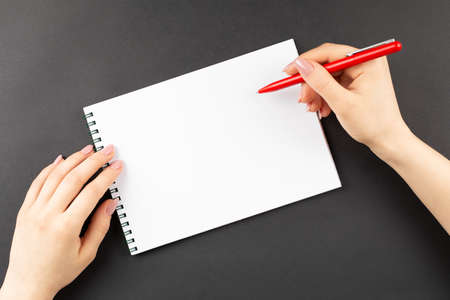 young woman hands hold opened notebook pages with red pen at dark table, top view. to-do list. doctor writes note,  shopping list. action plan on notepadの写真素材