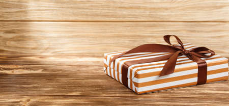Gift box with brown ribbon on wooden background top view. New year and Christmas holiday concept. Flat lay with copy space. Discount gift for sale day.の写真素材