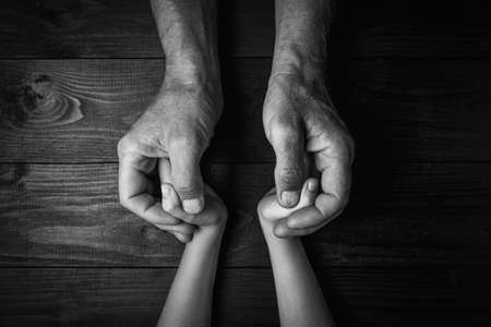 Top view, Hands of an elderly man holding the hand of a younger man. Lots of texture and character...