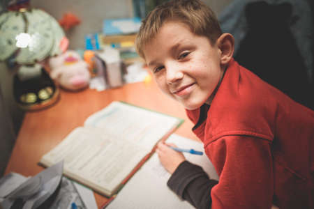child doing homework under the light of a lamp in a dark room. dark photo with lots of noise and...