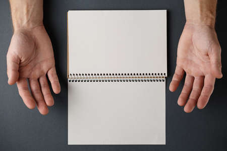 Open spiral notepad and male hands palms up on a gray background top view.
