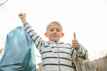 little boy in the park collect plastic bottles in a plastic bag, child scavenge on the...