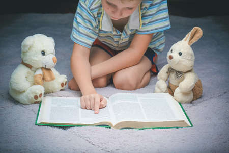 cute little boy reading book with his favorite toys on a soft plush blanketの写真素材