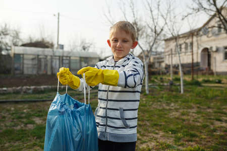 little boy in the park collect plastic bottles in a plastic bag, child scavenge on the streets.Environmental consciousness and awareness.の写真素材