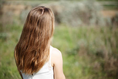 girl with beautiful hair is standing with her back in the field, sad girl