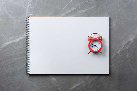 Spiral notebook with red alarm clock on marble table. Notepad goals plans dreams, make to do list...