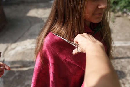 Teenage girl gets her hair cut outdoors in the fresh air during the day.の写真素材