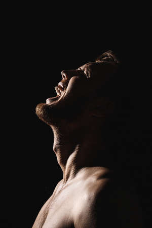 Man screaming with his head thrown back Concept of despair, fear and horror on a black isolated background.の写真素材