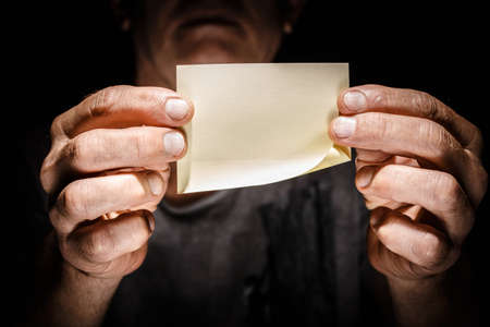 Blank scrap of craft paper in male hands on a black isolated background Scrapbook message concept.の写真素材