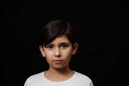 Portrait of cute little girl with pensive facial expression on black isolated background.
