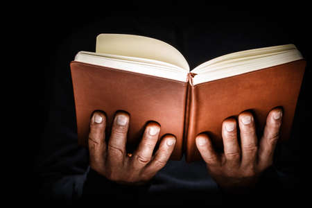 Male hands are holding an open hardback book on a black isolated background.