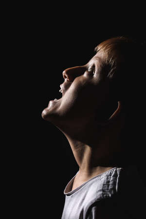 Boy screaming with his head thrown back Concept of despair, fear and horror on a black isolated background.の写真素材