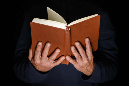 Male hands are holding an open hardback book on a black isolated background.の写真素材