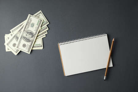 Open spiral notepad with a pencil and a stack of money on a gray background.の写真素材