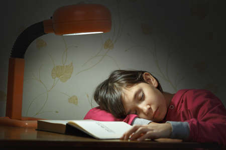 Little girl in a pink sweater fell asleep in the evening with her textbooks doing her homework by...