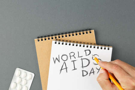 Open spiral notebook with clear page and male hands with pencil and tablet blister on grey background. First december World AIDS Day Cancer Control concept Symbolizing day of AIDS and HIV. Top view.の写真素材