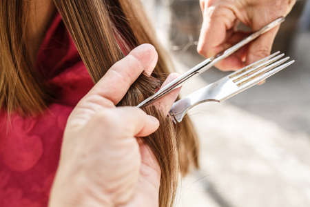 Young girl do hairstyle with a sunny day outdoors using a comb and scissorsの写真素材
