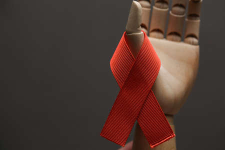 AID red ribbon in wood hand on gray dot background, symbol of the fight against HIV, AIDS and...