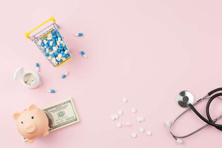 Pills with stethoscope and piggy bank on pink deskの写真素材