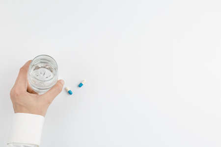 Hand with glass of water and pill white backgroundの写真素材
