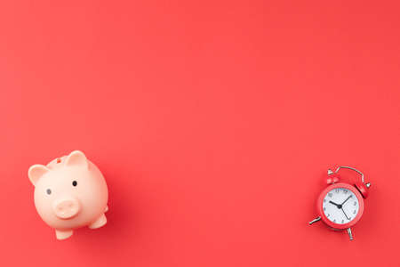 Red alarm clock and pink pig piggy bank.