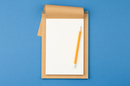 Open notebook with white blank sheet and pencil on blue isolated background. Top view.の写真素材