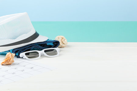 Vacation calendar at the sea on white wooden background. Summer holiday concept. Decoration of starfish and seashells. Beach hat with sunglasses.の写真素材