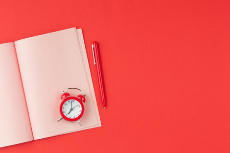 Pink open notebook with alarm clock and pen on red isolated background top view.の写真素材