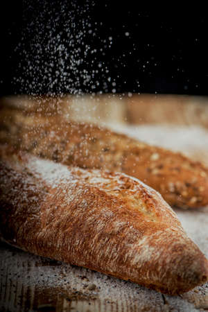 Vertical closeup view of two fresh crunchy baguettes with raining flour on the rustic wooden desk with seedsの写真素材