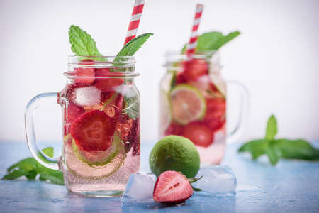 Close up view on lime and strawberry detox drink in glass mason jars on a blue background. A wellness summer lemonade.の写真素材