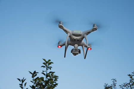 White quadrocopter is flying high in the air, taking photos, recording footage from above. Drone...