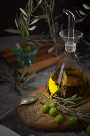 Extra virgin olive oil in glass bottle with branch of olives on rustic background. low key. side viewの写真素材