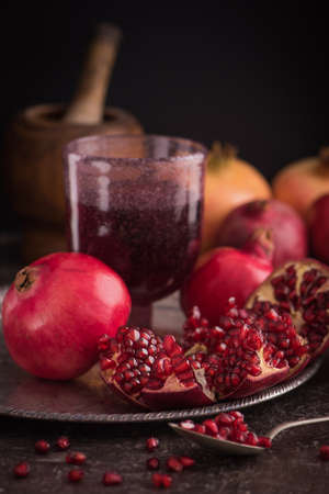 A glass of pomegranate juice with fresh pomegranate fruits and seeds on rustic background. Side view. Low keyの写真素材