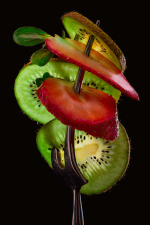 Sliced fresh and juicy green kiwi and red strawberry on the silver fork on dark background. healthy food concept. close up. low key.の写真素材