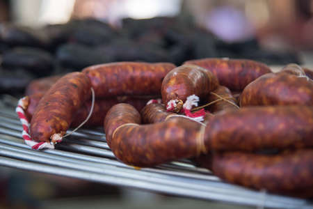 Different kinds of fresh spanish sausages on big round grill and hanging in bunches. Close up. Soft focus.の写真素材
