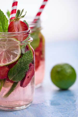Close up view on lime and strawberry detox drink in glass mason jars on a blue background. A wellness summer lemonade.の写真素材