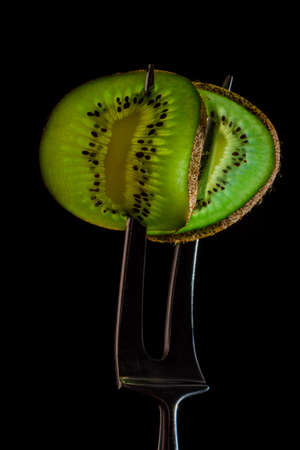 Sliced fresh and juicy green kiwi on the silver fork on dark background. healthy food concept. close...