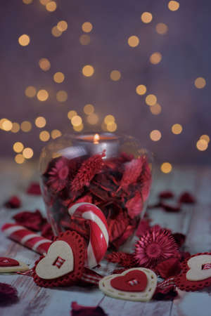 Closeup view glass candle holder with christmas or valentine hearts and candy on rustic background and falling sparks, selective focus.の写真素材