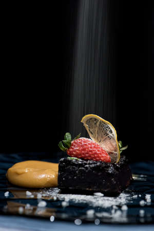 Black currant cake with salted caramel and strawberry with falling sour sugar flour side viewの写真素材