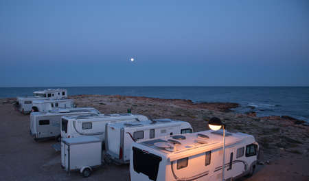 A camp of caravan cars and motor homes parked on the seaside of mediterranean sea at young night....