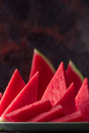 Fresh sweet spanish watermelon sliced on green plate on dark background. Low key close up shot with...